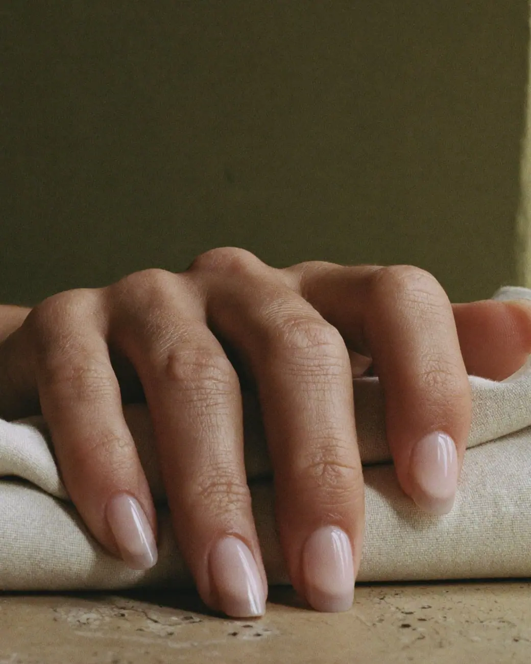 Conceptual image: fingertips with sheer nude almond nails resting on folded linen