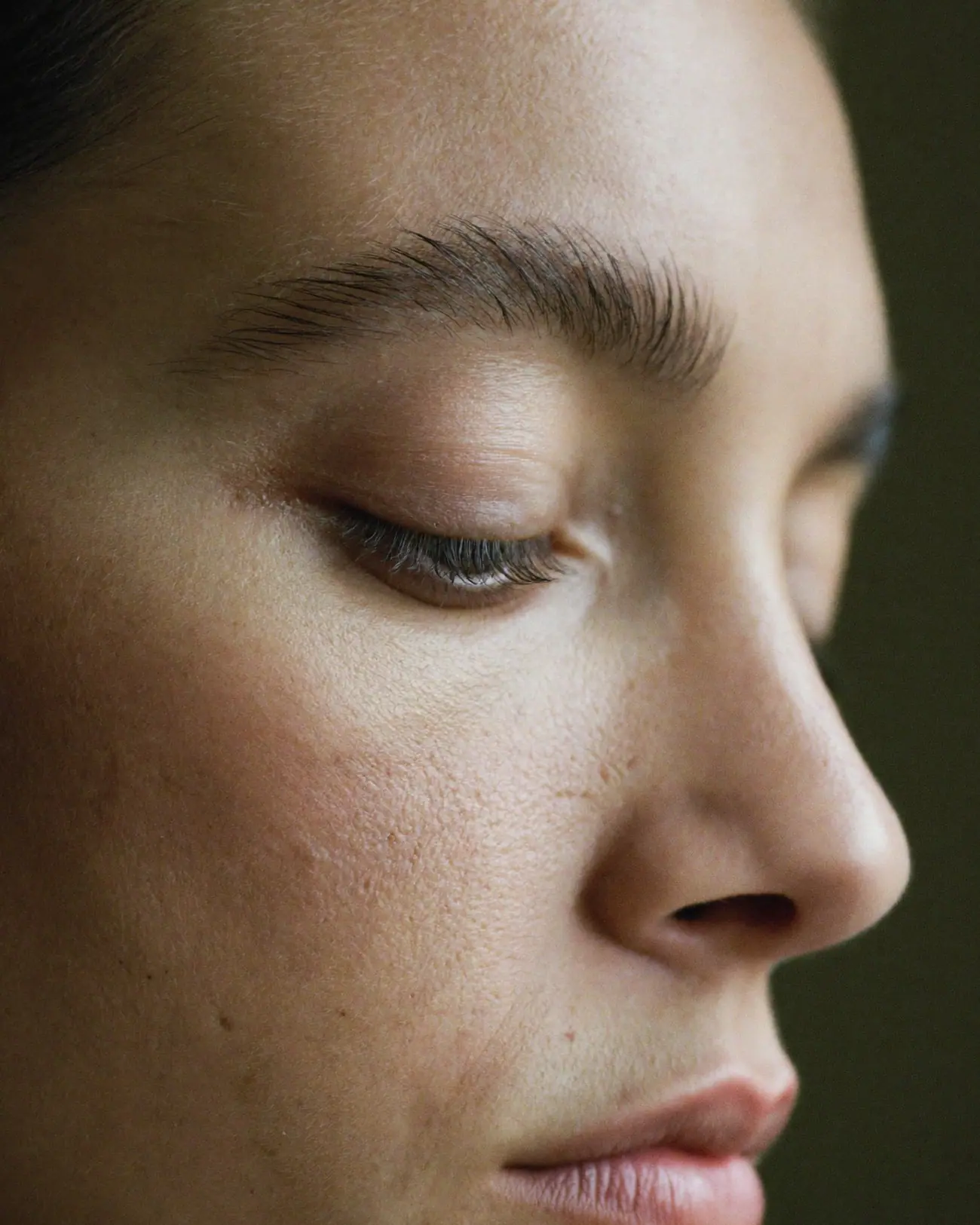 Conceptual image: close-up of a naturally groomed eyebrow and lowered eye in soft profile